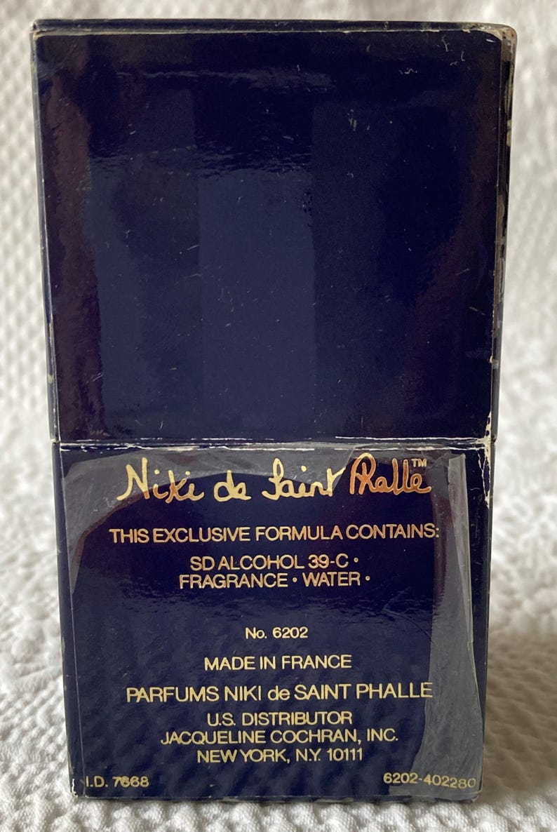 Puede incluir: Una caja azul con letras doradas para el perfume Niki de Saint Phalle. La caja tiene el texto "This exclusive formula contains: SD Alcohol 39-C. Fragrance. Water." y "No. 6202 Made in France Parfums Niki de Saint Phalle U.S. Distributor Jacqueline Cochran, Inc. New York, N.Y. 10111 6202-402280".