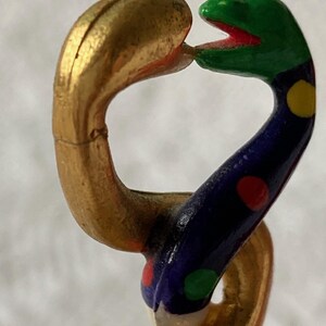 Puede incluir: Una cadena de serpiente dorada y multicolor con una cabeza verde y una boca roja. La serpiente est&aacute; decorada con lunares azules, rojos, amarillos y verdes.