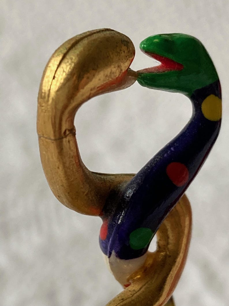 Puede incluir: Una cadena de serpiente dorada y multicolor con una cabeza verde y una boca roja. La serpiente est&aacute; decorada con lunares azules, rojos, amarillos y verdes.