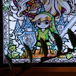 Puede incluir: Una ventana de vitral que representa a Link de la serie de videojuegos The Legend of Zelda. Link sostiene una espada y un escudo, y est&aacute; de pie frente a un castillo. La ventana est&aacute; enmarcada en negro y tiene un fondo azul claro.