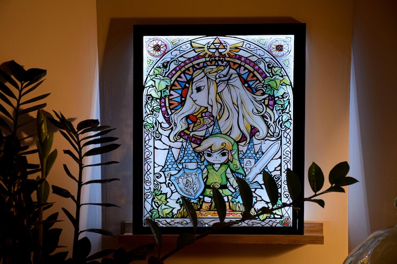 Puede incluir: Una obra de arte enmarcada de estilo vitral que representa una versi&oacute;n de dibujos animados de Link y Zelda de la serie de videojuegos The Legend of Zelda. La obra est&aacute; retroiluminada, creando un brillo colorido.