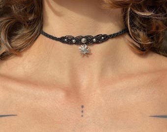 Puede incluir: Un collar gargantilla negro con un dije de sol plateado. El collar está hecho de un cordón delgado trenzado con pequeñas cuentas plateadas.