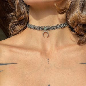 Peut inclure: Un collier ras de cou en macramé gris avec un pendentif en forme de croissant de lune et un accent de pierre verte.
