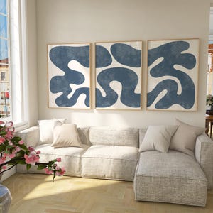 Minimalist navy blue prints in light wood frames above a sectional sofa in a bright, modern open-concept living room.