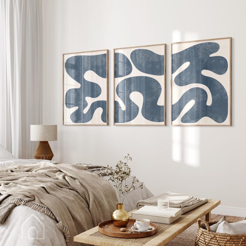 Three navy blue abstract prints hanging above a bed with neutral linens, creating a calm master bedroom atmosphere.
