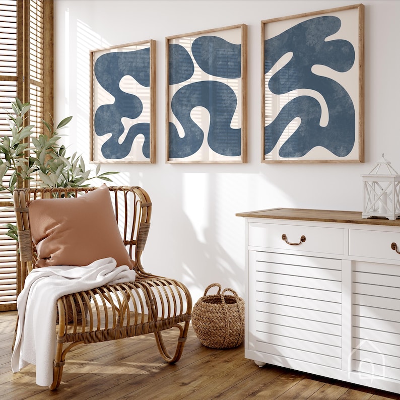 Coastal navy blue wall art set hanging in a sunlit room next to a rattan chair and a white dresser.