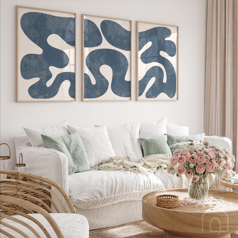 Navy blue triptych prints above a white sofa in a bright living room styled with pink flowers and green cushions.
