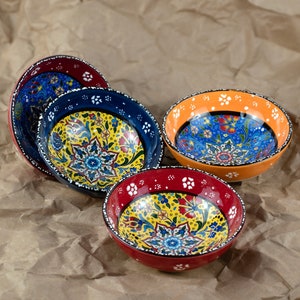 May include: Four ceramic bowls with colorful floral patterns. The bowls have a variety of colors, including blue, red, orange, and yellow. The bowls are arranged on a brown paper surface.