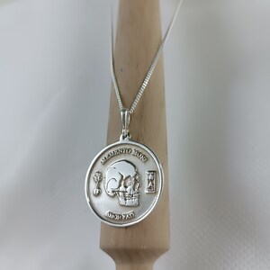 May include: Silver necklace with a round pendant featuring a skull, an hourglass, and the words "Memento Mori" and "Amor Fati".