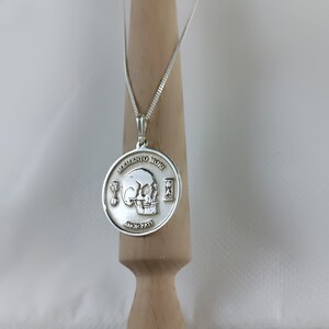 May include: A silver necklace with a round pendant featuring a skull and the words "Memento Mori" and "Amor Fati".
