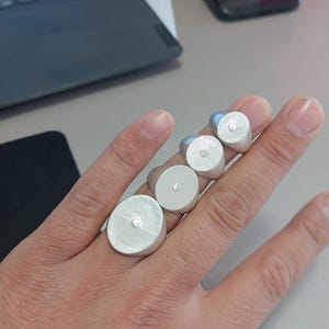 Puede incluir: Cuatro anillos de sello de plata con una pequeña piedra redonda engastada en el centro de cada anillo. Los anillos se llevan en los dedos de una mano.