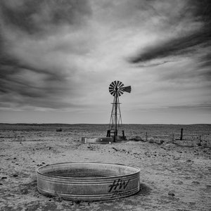 May include: A black and white photo of a windmill in a field with a large metal water trough. The trough has the letters "HW" and "TRUCK" printed on it.