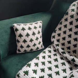 Könnte beinhalten: Eine weiße Häkeldecke und ein Kissen mit grünem Baummuster. Die Decke und das Kissen liegen auf einem grünen Sofa.