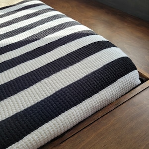 Könnte beinhalten: Ein schwarzes und weißes gestreiftes Stoffkissen auf einer Holzbank.