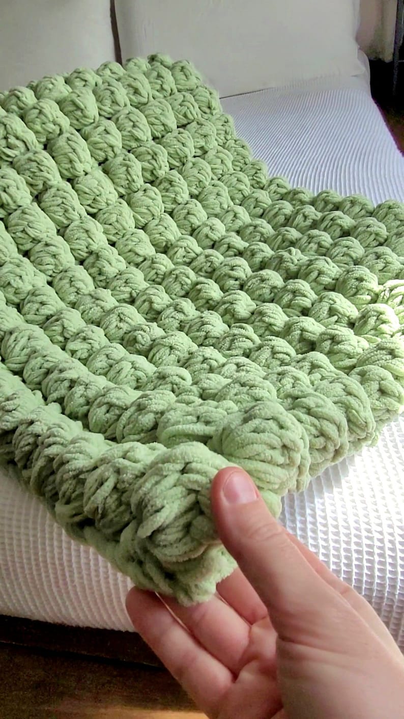 Op de afbeelding: Een zacht, groen gebreid deken met een textuur, een bolletjes ontwerp. Het deken is gemaakt van dik garen en heeft een pluche, zachte uitstraling.