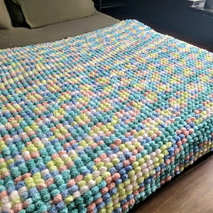 May include: A soft, colorful blanket made of fluffy pom-poms in shades of pink, blue, green, and yellow.
