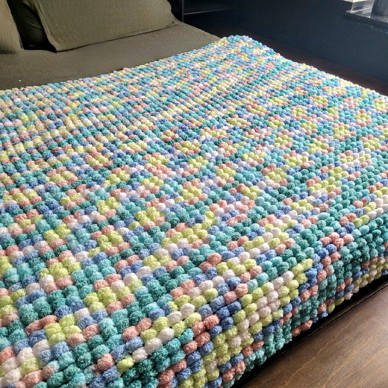 May include: A soft, colorful blanket made of fluffy pom-poms in shades of pink, blue, green, and yellow.