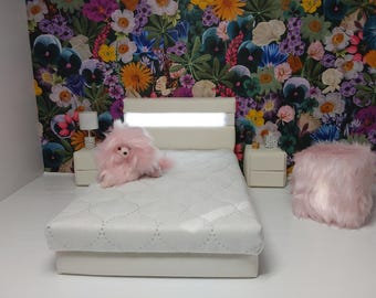 Könnte beinhalten: Ein Miniatur-Schlafzimmer-Set mit einem weißen Bett, Nachttischen und einem flauschigen rosa Hocker. Das Bett hat ein weißes Kopfteil mit eingebauter Beleuchtung. Ein rosa Stofftier sitzt auf dem Bett. Die Tapete hat ein farbenfrohes Blumenmuster.