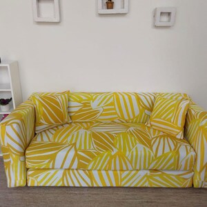 May include: A miniature yellow and white patterned sofa with two matching pillows. The sofa has a modern design and is likely for a dollhouse or other miniature setting. The fabric features a leaf-like pattern.
