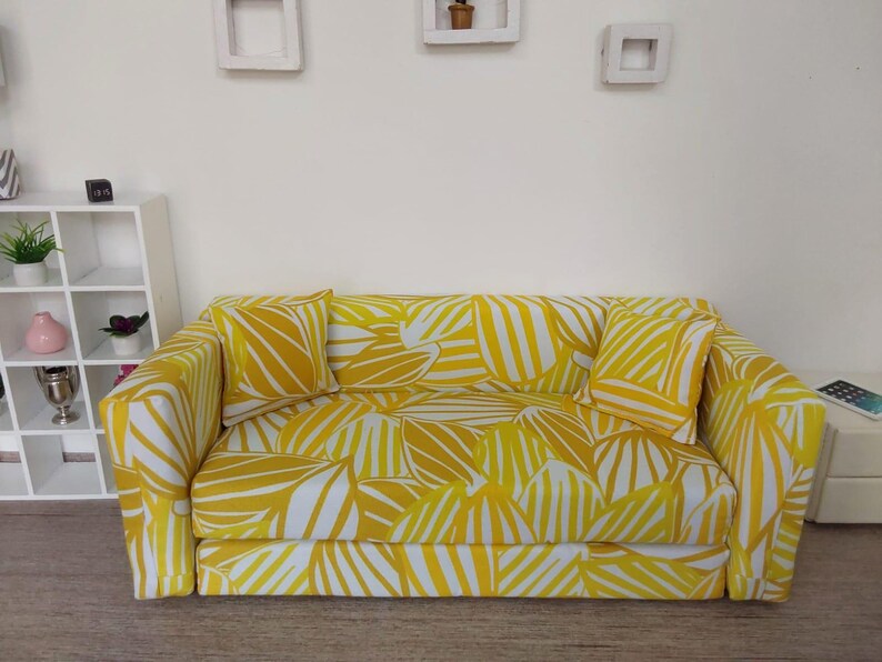 May include: A miniature yellow and white patterned sofa with two matching pillows. The sofa has a modern design and is likely for a dollhouse or other miniature setting. The fabric features a leaf-like pattern.