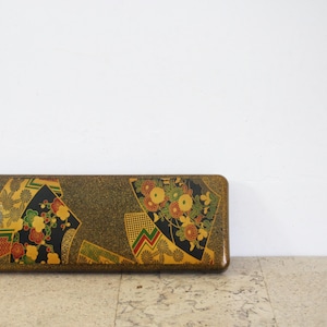 Può includere: Scatola giapponese rettangolare vintage con base marrone scuro e motivi floreali e geometrici decorativi in nero, oro, verde e rosso. La scatola è in legno e ha una finitura lucida.
