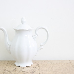 Pode incluir: Uma chaleira de porcelana branca com corpo canelado e uma alça delicada. A chaleira tem um design clássico e é perfeita para servir chá.