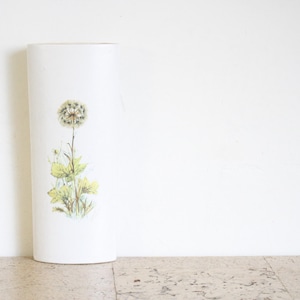 May include: A white cylindrical vase featuring a dandelion illustration. The dandelion has a fluffy seed head, green leaves, and a stem. The vase is approximately 25 cm tall.