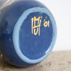 May include: Blue ceramic vase with a white and yellow floral design. The bottom of the vase has a light blue ring and the number "01" written in yellow.