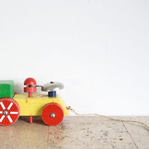 May include: A vintage wooden toy train with a green block, yellow body, and red wheels. The train features a red bell and a silver dome. A string is attached for pulling the toy.