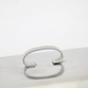 Puede incluir: Una bandeja de servicio de metal plateado brillante con un asa curva. La bandeja tiene forma rectangular y una superficie reflectante, creando un efecto de espejo. El asa tiene un dise&ntilde;o simple y arqueado.