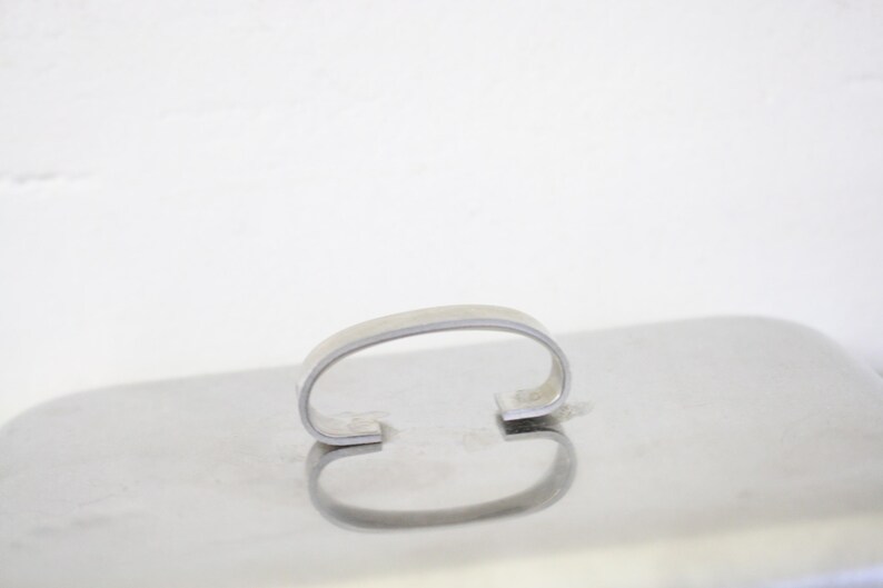 Puede incluir: Una bandeja de servicio de metal plateado brillante con un asa curva. La bandeja tiene forma rectangular y una superficie reflectante, creando un efecto de espejo. El asa tiene un dise&ntilde;o simple y arqueado.