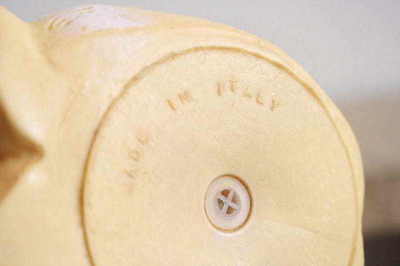 May include: Close-up of the bottom of a cream-colored ceramic figurine. The figurine has a small hole in the bottom and the words "MADE IN ITALY" are embossed on the bottom.