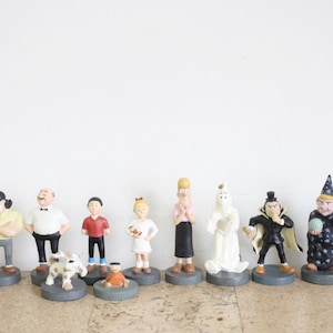 May include: A collection of 11 figurines, including a dog, a ghost, a witch, and several people. The figurines are all painted in various colors and are standing on small bases.