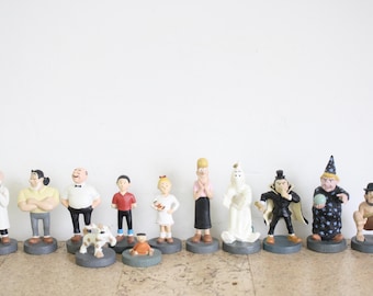 May include: A collection of 11 figurines, including a dog, a ghost, a witch, and several people. The figurines are all painted in various colors and are standing on small bases.