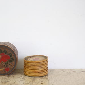 Peut inclure: Un ensemble de sous-verres en bois avec un motif floral. Les sous-verres sont empilés les uns sur les autres et sont en bois brun clair. Il y a une boîte ronde en bois avec un motif floral sur le côté.