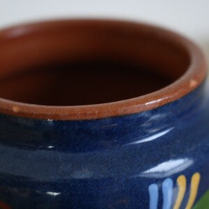 May include: A blue ceramic jar with a brown rim and painted floral designs in yellow, blue, and green.