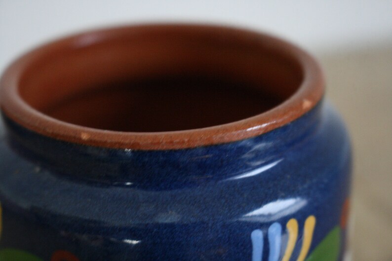 May include: A blue ceramic jar with a brown rim and painted floral designs in yellow, blue, and green.
