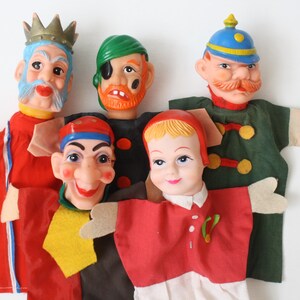 Op de afbeelding: Een verzameling van vijf handpoppen met diverse personages, waaronder een koning met een kroon, een piraat met een ooglapje, een soldaat met een snor, een nar en een kind. Elke pop heeft een beschilderd gezicht en kleding van stof.