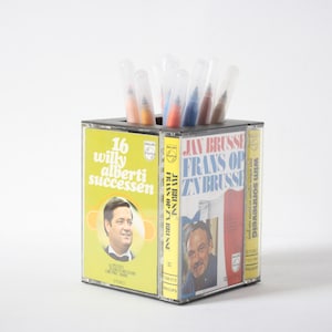 May include: A black cassette tape holder with a yellow, blue, and red cassette tape design. The holder is filled with colorful markers.