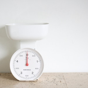 May include: White kitchen scale with a red needle and a white bowl on top. The scale has a black dial with numbers 1 through 4 and 500g markings. The scale is made by Soehnle.