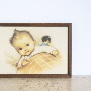 May include: A framed illustration of a baby in a crib with a doll lying beside them. The baby is wearing a white onesie and the doll is wearing a blue dress. The illustration is done in a soft, pastel color palette.