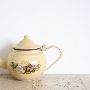 以下が含まれることがあります： クリーム色のエナメルティーポット。茶色、白、オレンジ色のバラの花柄。 ティーポットは、曲がったハンドル、注ぎ口、蓋が付いています。 リムとハンドルは濃い茶色で縁取られています。