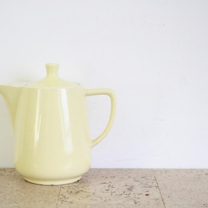 Puede incluir: Una tetera de cerámica de color amarillo pálido con un cuerpo redondeado y un pico en el lateral. La tetera tiene una tapa y un asa.