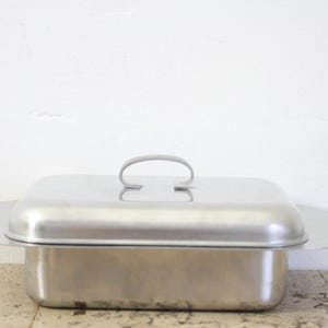 Puede incluir: Una fuente rectangular de acero inoxidable con tapa a juego y asa curvada. La fuente tiene un dise&ntilde;o sencillo y funcional y es adecuada para servir alimentos. La tapa tiene un asa ligeramente elevada para facilitar su elevaci&oacute;n.
