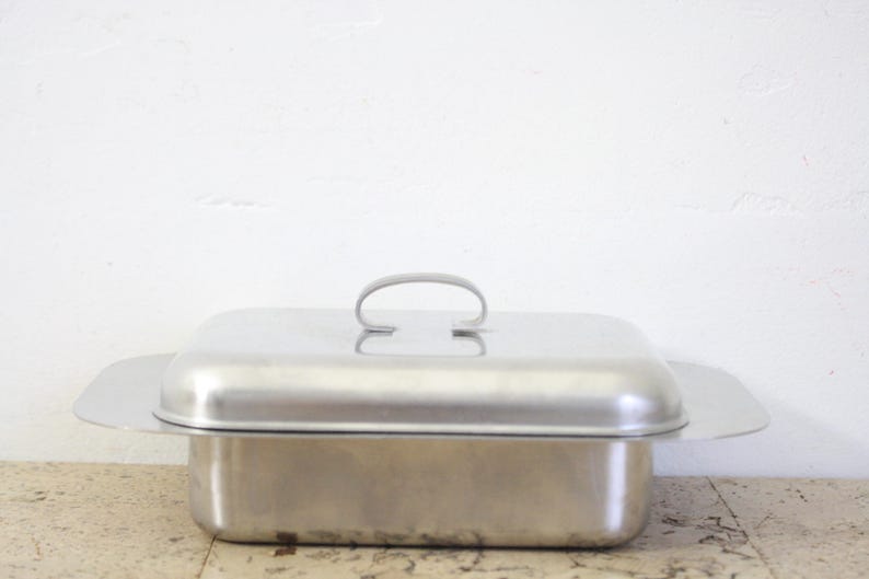 Puede incluir: Una fuente rectangular de acero inoxidable con tapa a juego y asa curvada. La fuente tiene un dise&ntilde;o sencillo y funcional y es adecuada para servir alimentos. La tapa tiene un asa ligeramente elevada para facilitar su elevaci&oacute;n.