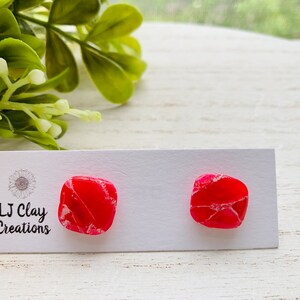 May include: A pair of pink and white square-shaped earrings on a white card with the text "LJ Clay Creations".