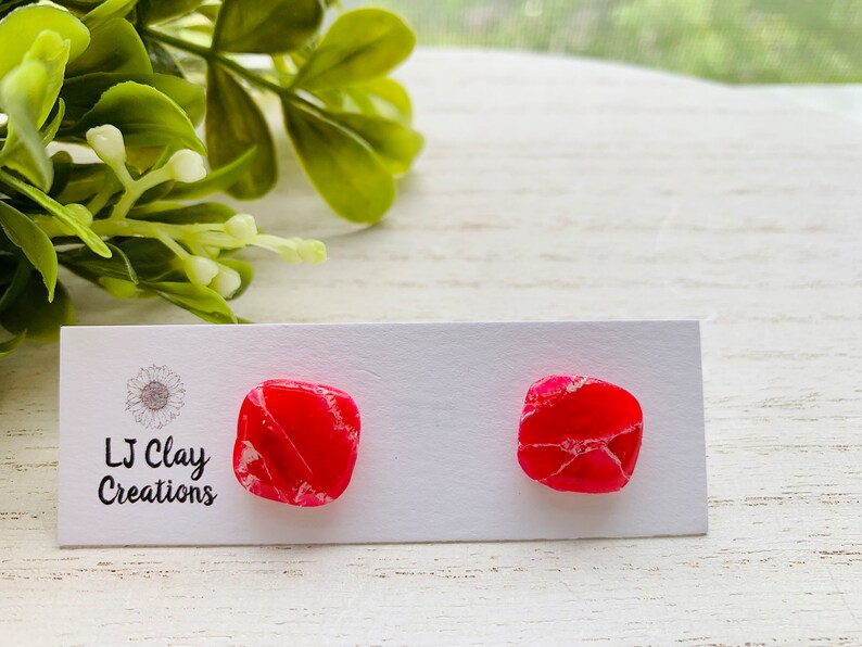 Puede incluir: Un par de pendientes cuadrados de color rosa y blanco sobre una tarjeta blanca con el texto "LJ Clay Creations".