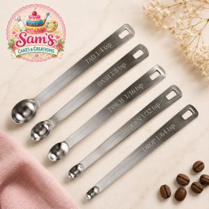May include: A set of five stainless steel measuring spoons with long handles and rectangular hanging holes. Each spoon is engraved with a specific measurement: TAD 1/4 tsp, DASH 1/8 tsp, PINCH 1/16 tsp, SMIDGEN 1/32 tsp, and DROP 1/64 tsp.