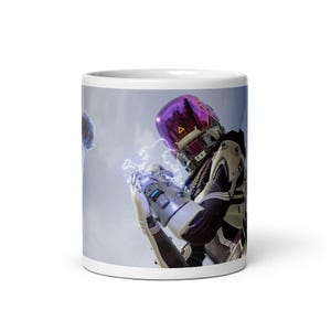 May include: White ceramic mug featuring a futuristic character with a purple helmet and silver armor, holding a glowing energy effect. The design is set against a cloudy sky background, creating a sci-fi theme.