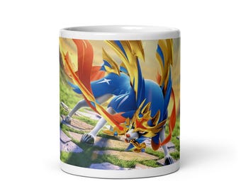 May include: White ceramic mug featuring a vibrant illustration of a blue and gold creature with a red cape, set against a background of green grass and a yellow sky. The creature is in a dynamic pose.